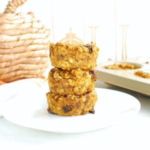 Three pumpkin baked oatmeal cups on a plate, next to a woven pumpkin decoration.