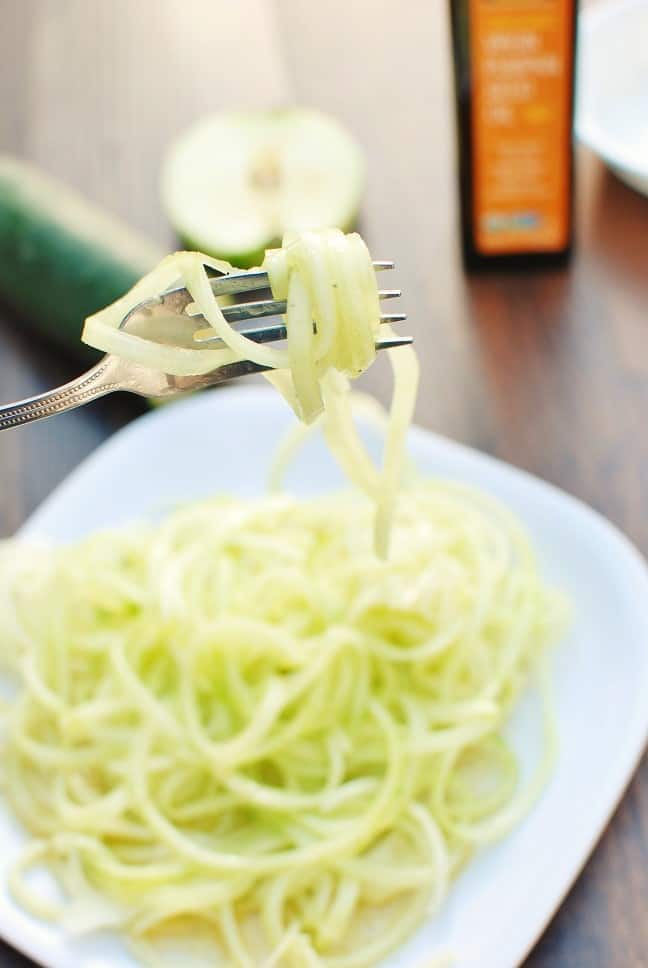 a woman twirling a fork that has spiralized apples and cucumbers on it