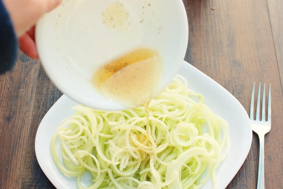 a woman pouring a pumpkin seed oil vinaigrette onto a cucumber apple salad