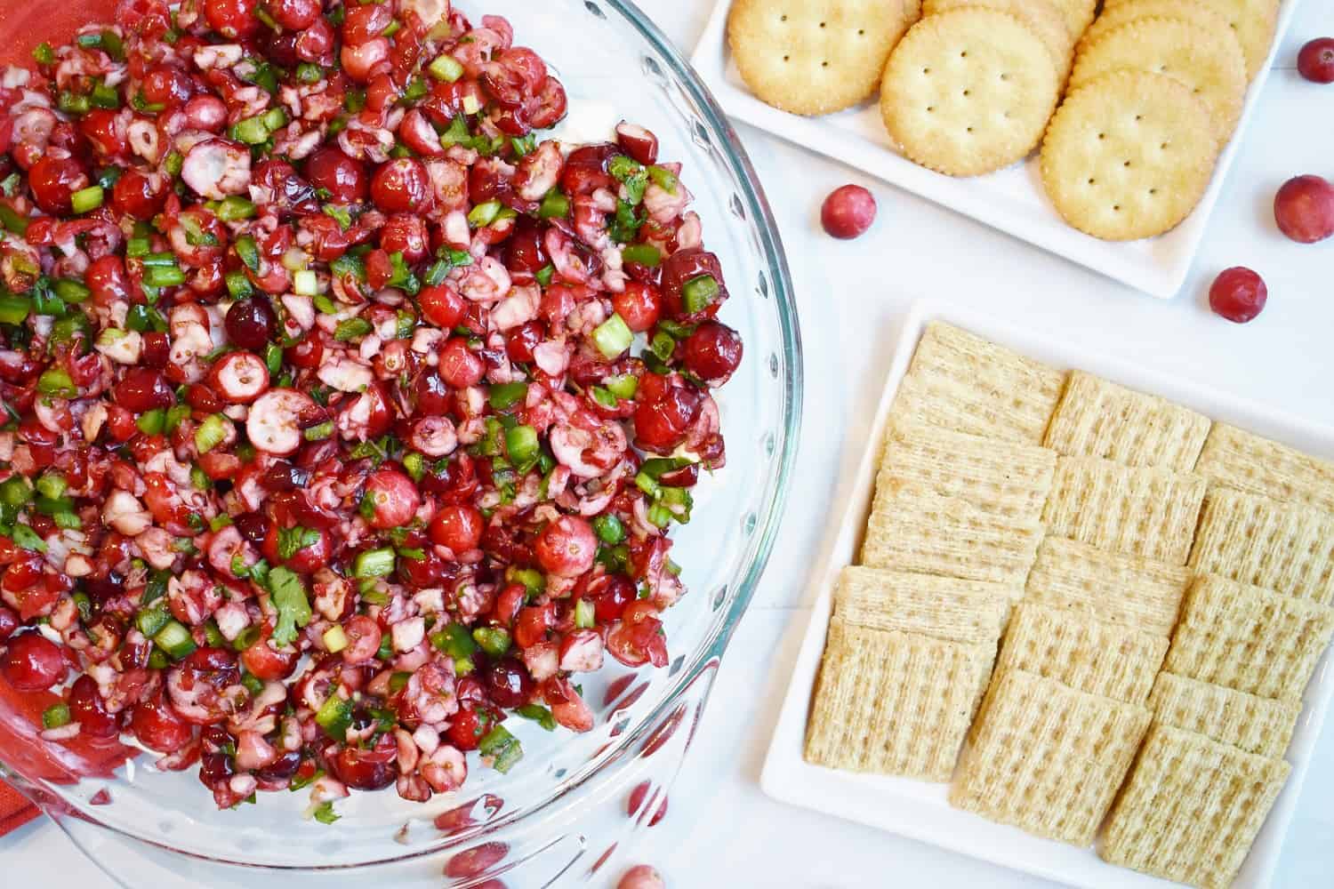 a pie plate filled with cranberry jalapeno dip next to a plate with some crackers