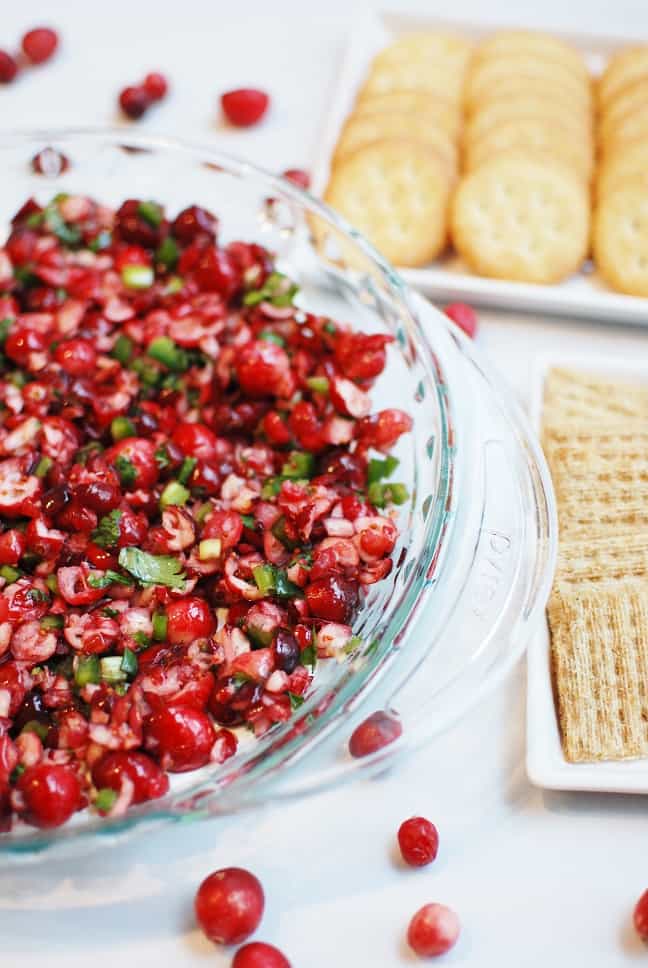 a platter with cranberry jalapeno cream cheese dip, next to two plates with two different kinds of crackers