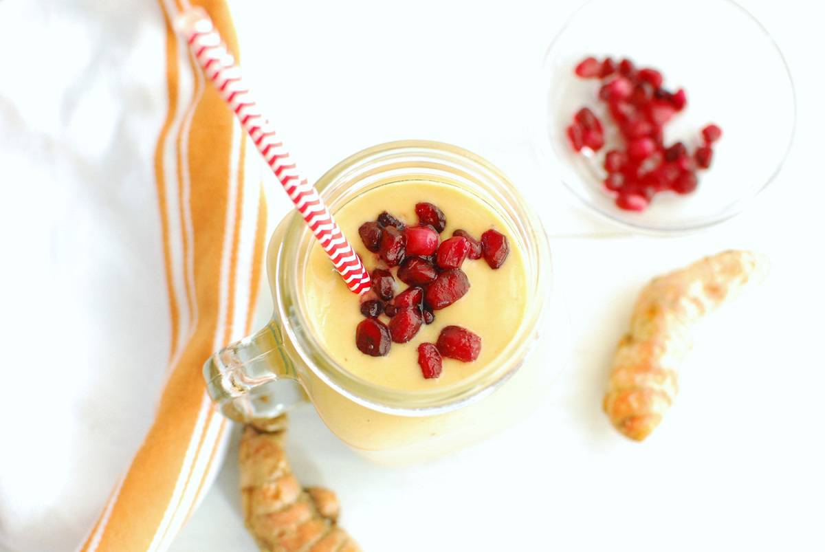 A turmeric smoothie garnished with pomegranate seeds.