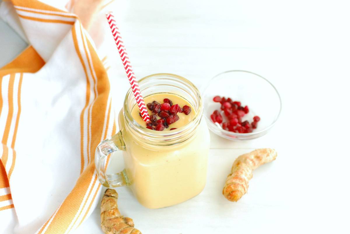 A turmeric banana smoothie in a glass mason jar next to a napkin and some fresh turmeric root.