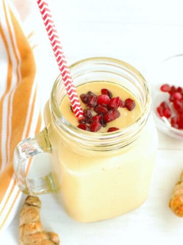 A turmeric banana smoothie next to fresh turmeric, pomegranate arils, and a napkin.