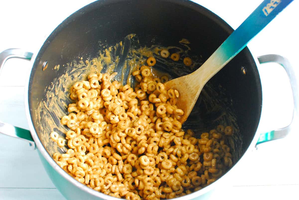 Cheerios stirred into the peanut butter honey mixture in the pot.