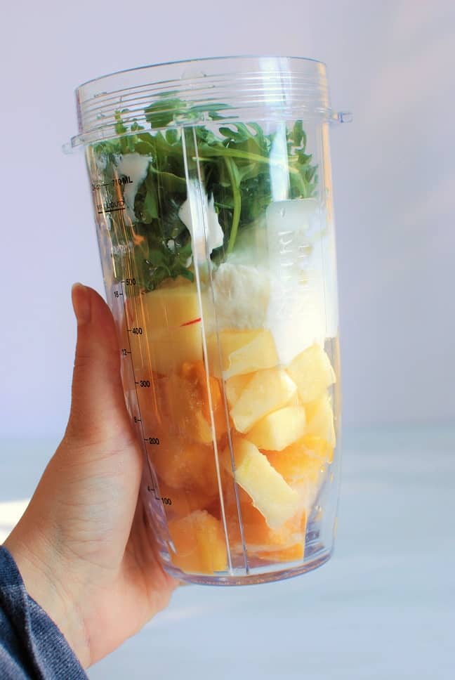 A blender cup filled with ingredients for an apple arugula smoothie