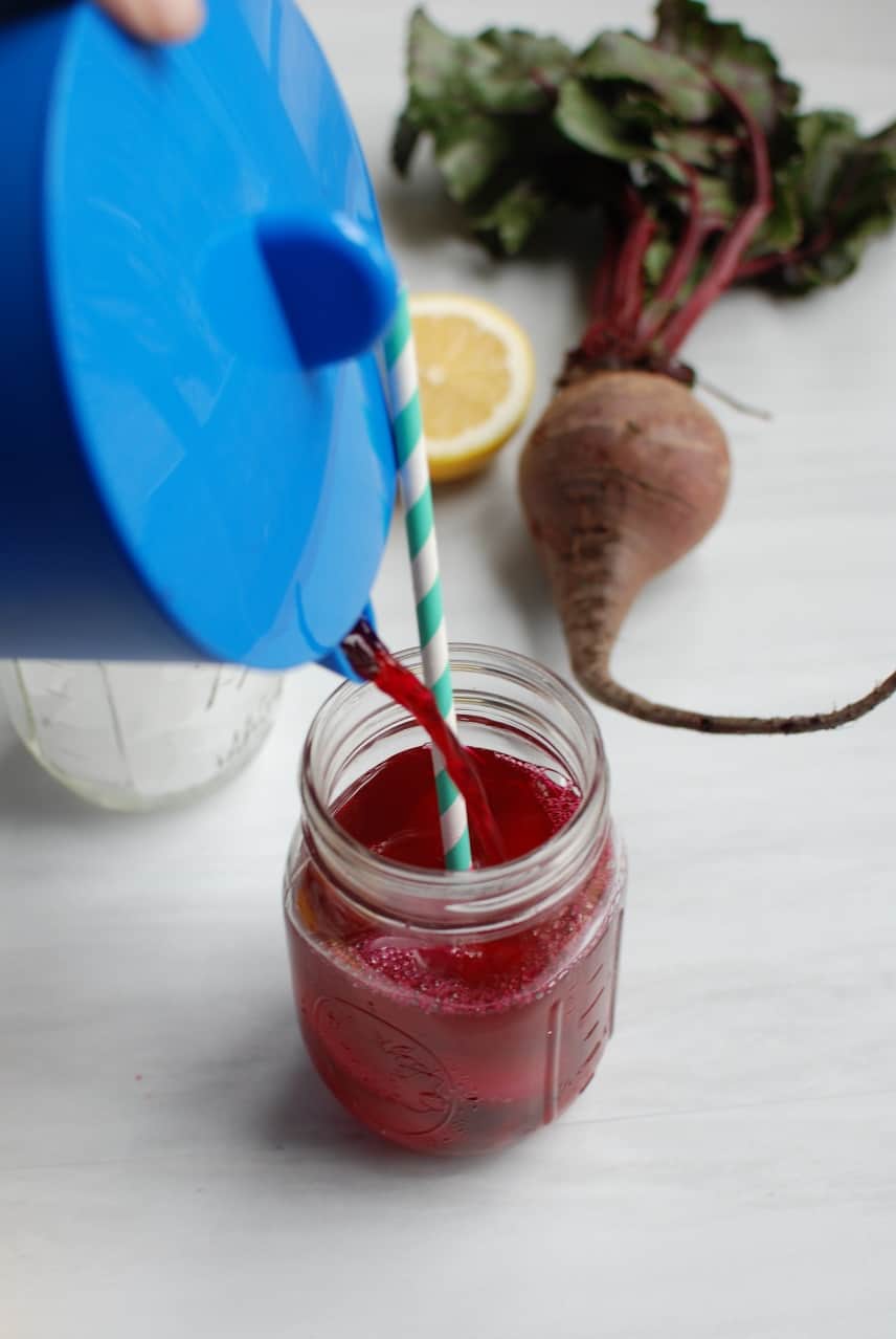 Blue pitcher pouring beet lemonade into a mason jar