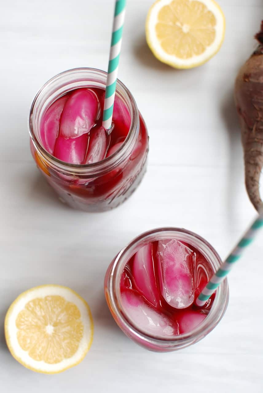 Mason jars filled with beet lemonade and ice cubes, next to a sliced lemon