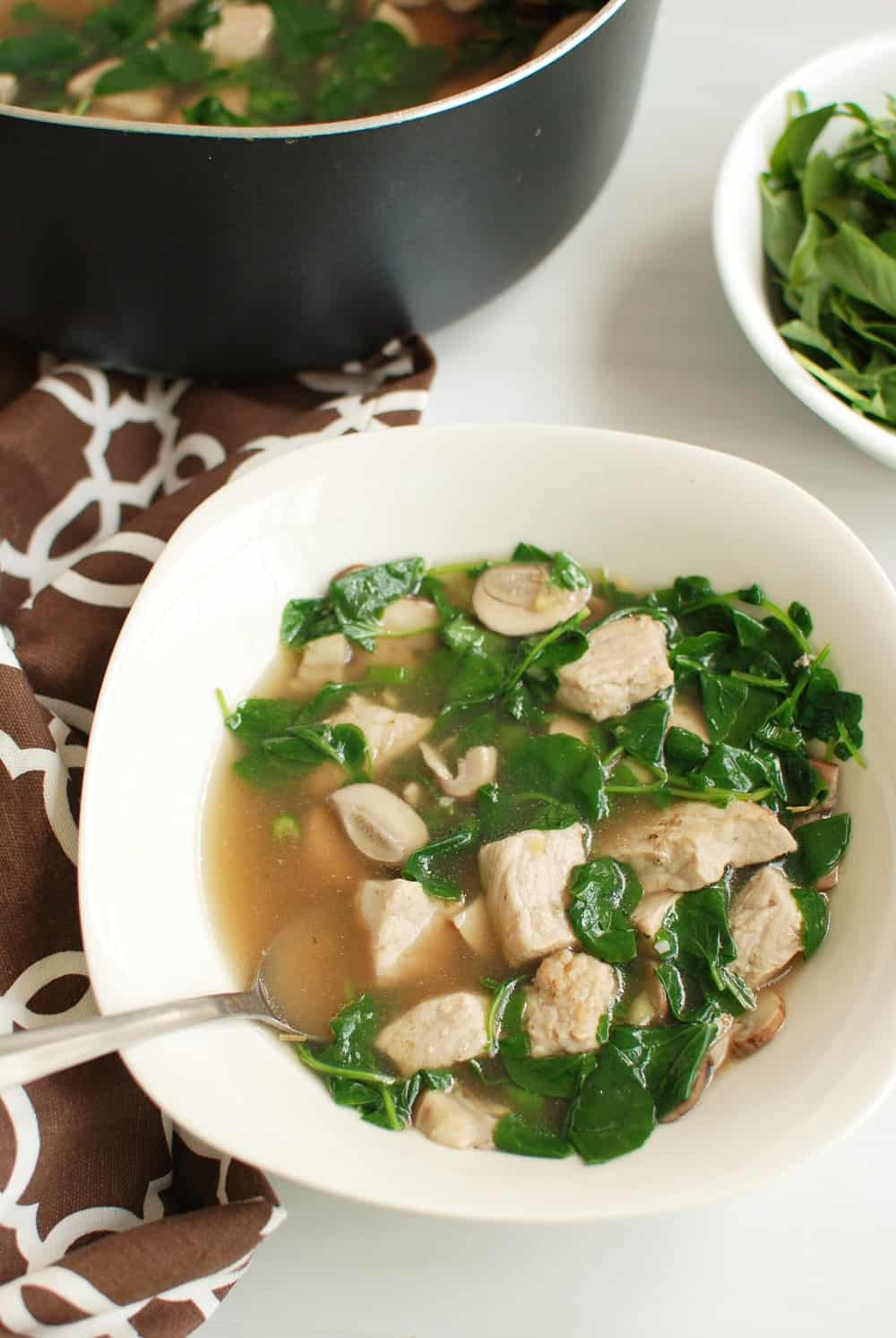 White bowl full of pork watercress soup next to a pot