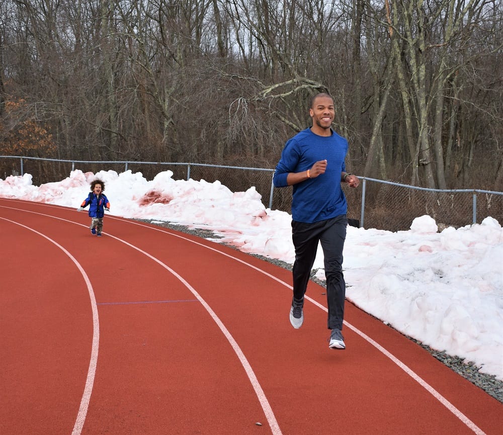 Man running on a track with his son chasing after him