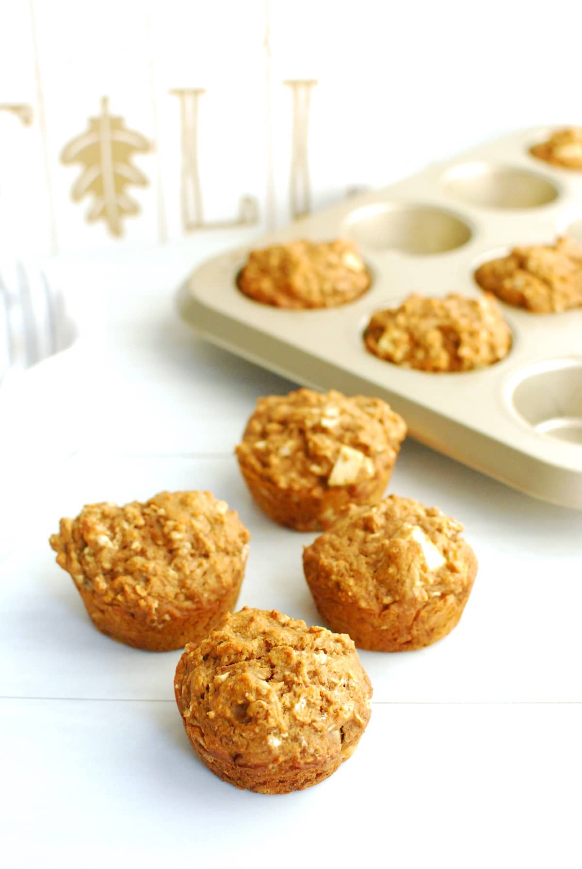 Several low sugar apple muffins on a table next to the baking tin and a fall sign.