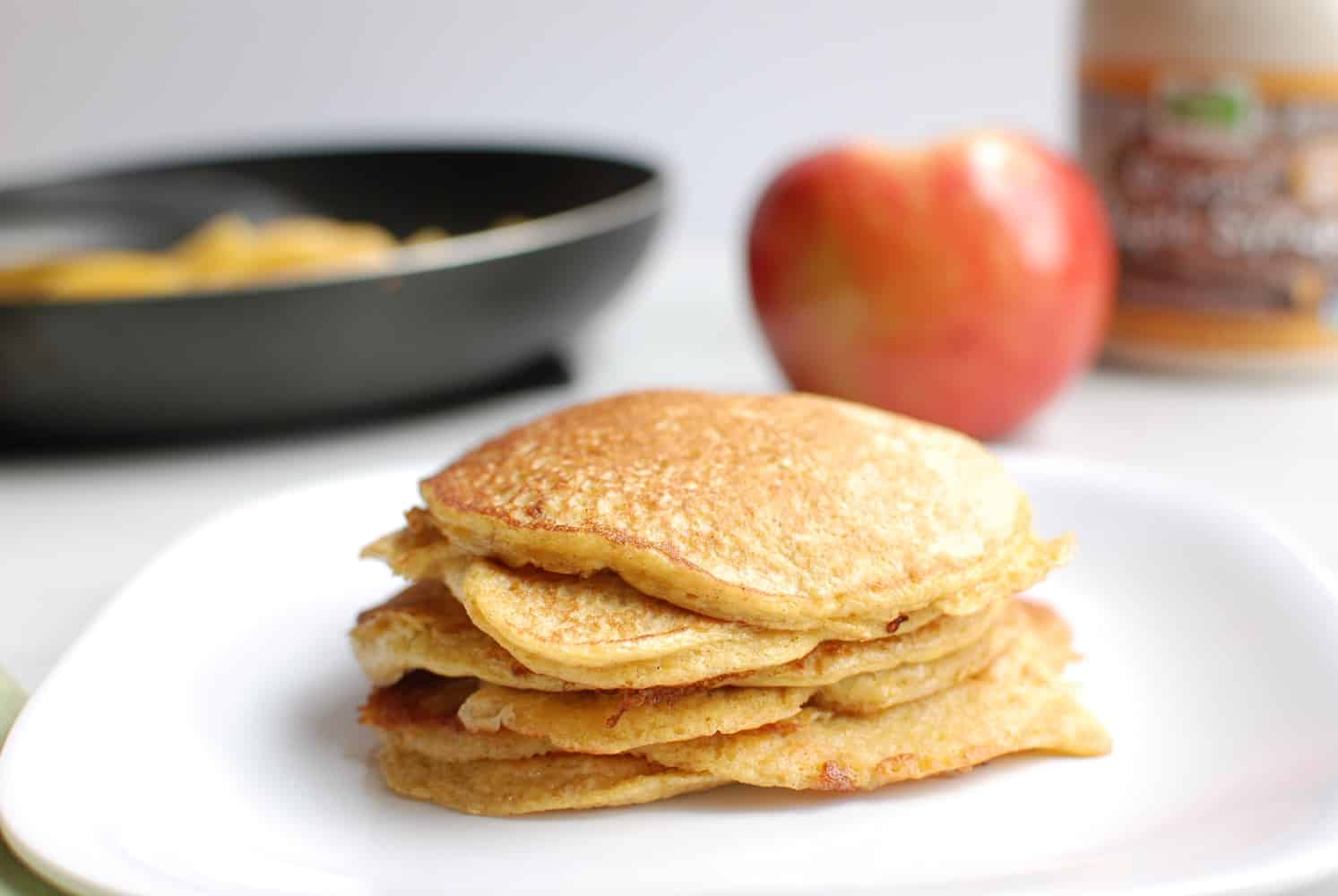 Cottage cheese protein pancakes on a white plate with an apple and maple syrup in the background.