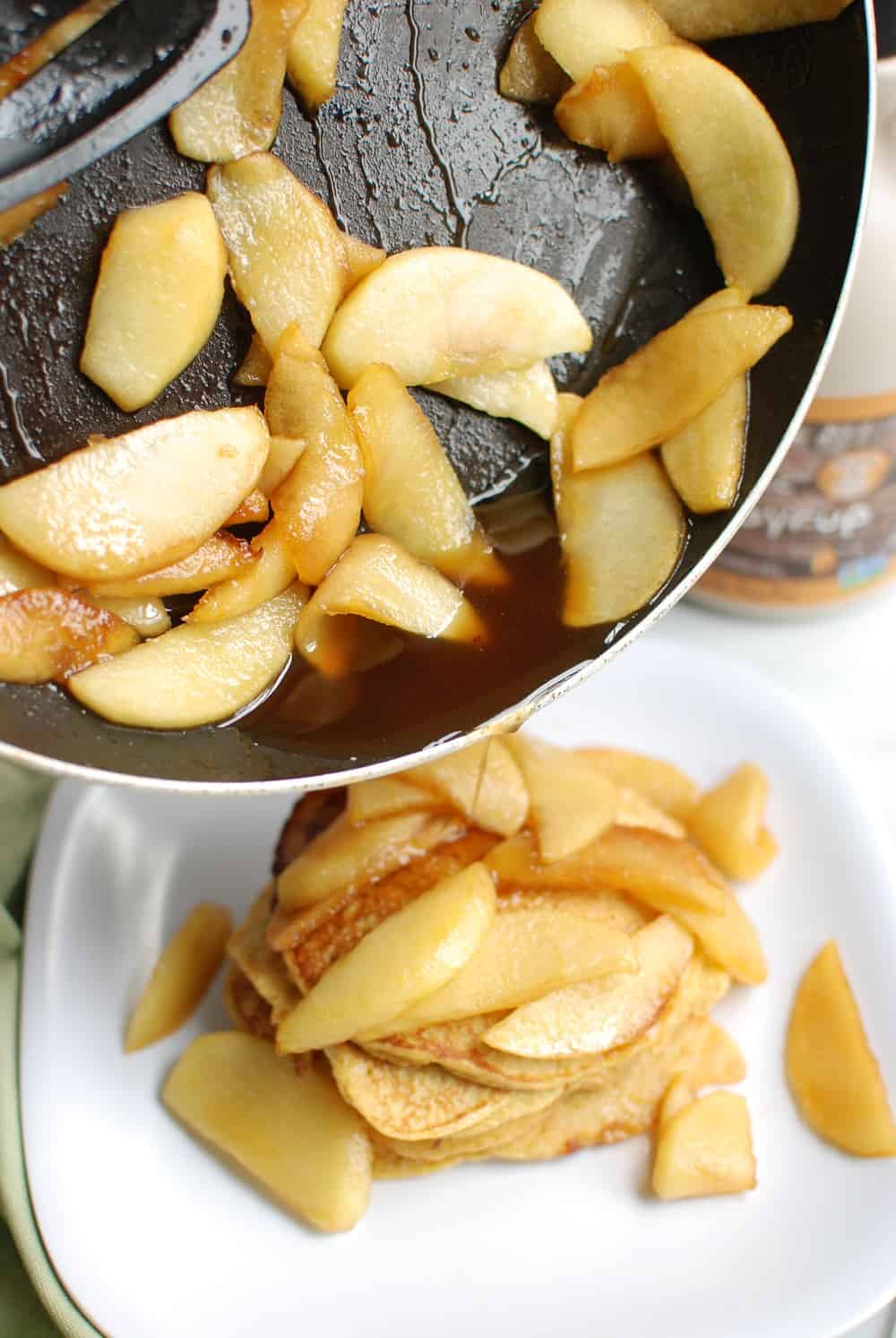 Sautéed apple topping in a pan being poured onto pancakes.