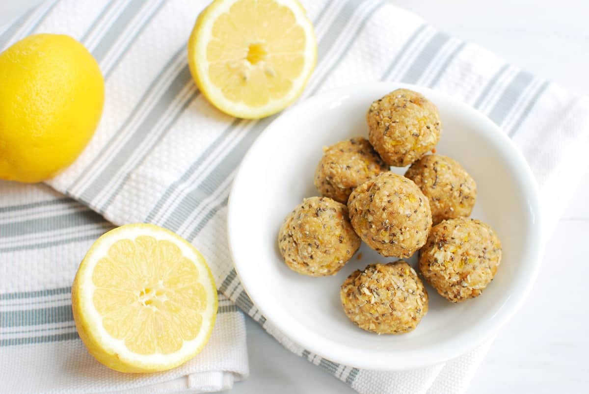 A bowl of lemon energy bites next to a napkin and sliced lemons.