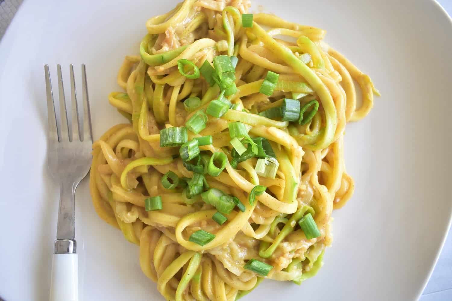 Almond butter zoodles garnished with scallions on a white plate.