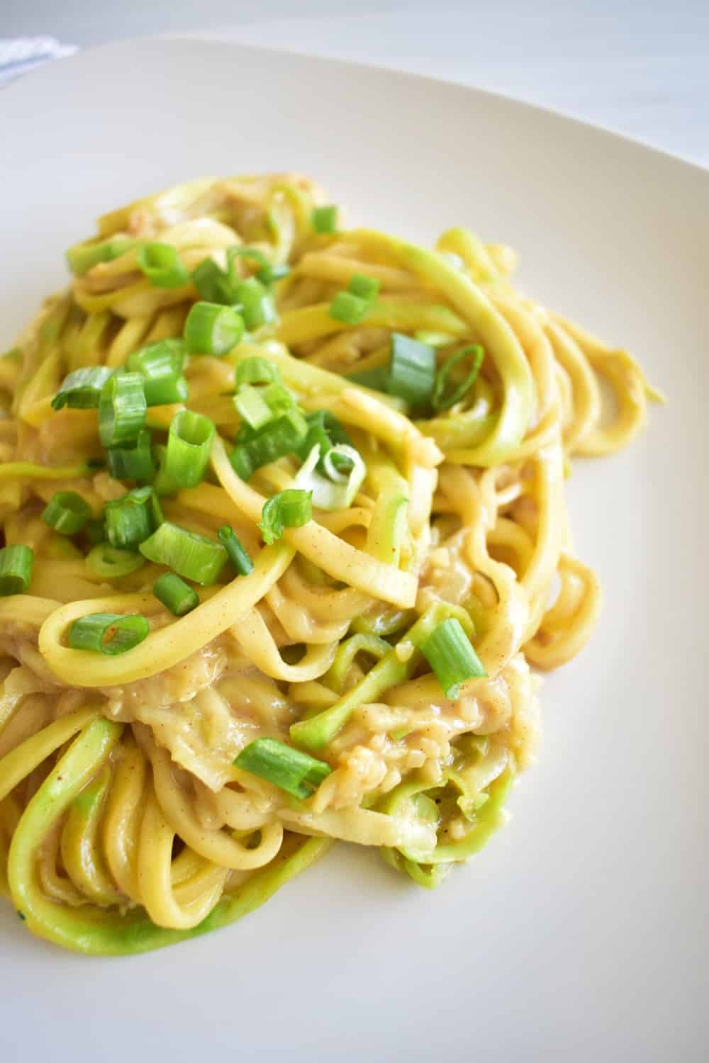 Zucchini noodles with almond butter sauce garnished with scallions.