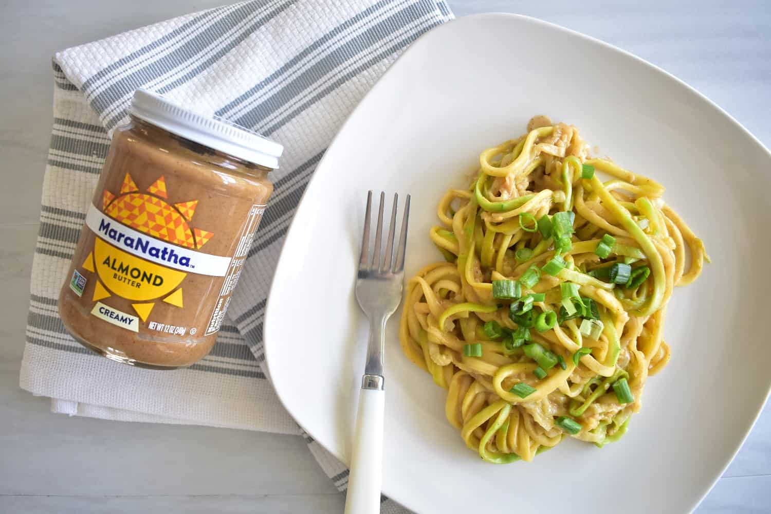 zucchini noodles with almond butter sauce on a plate next to a jar of almond butter