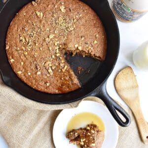 A cast iron skillet with banana bread baked in it, with a slice cut out and put on a plate.