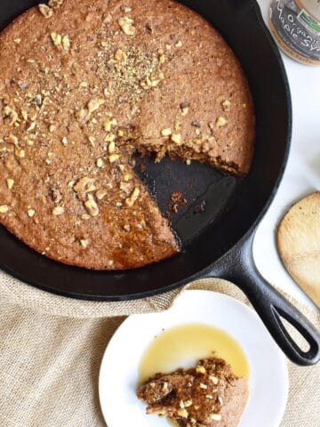 A cast iron skillet with banana bread baked in it, with a slice cut out and put on a plate.