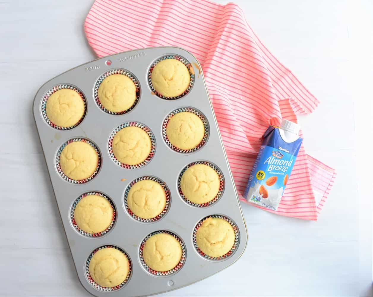 Pan of vegan vanilla cupcakes next to a container of almondmilk