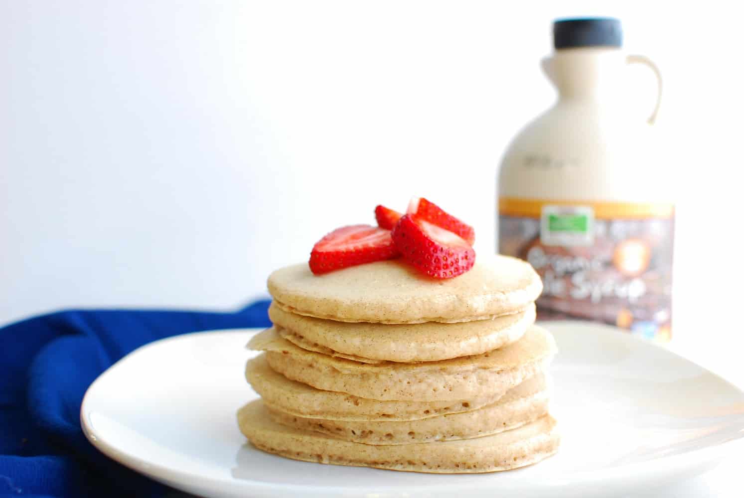 Several dairy free eggless pancakes on a plate topped with strawberries
