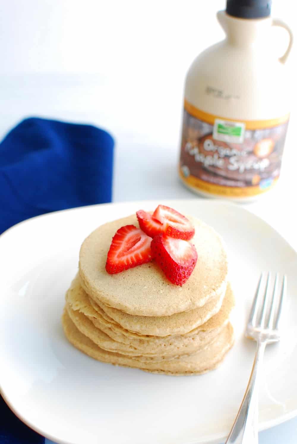 Stack of almond milk pancakes on a white plate next to maple syrup