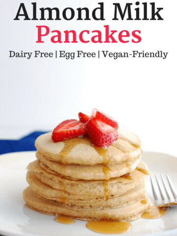 A stack of almond milk pancakes topped with strawberries and maple syrup