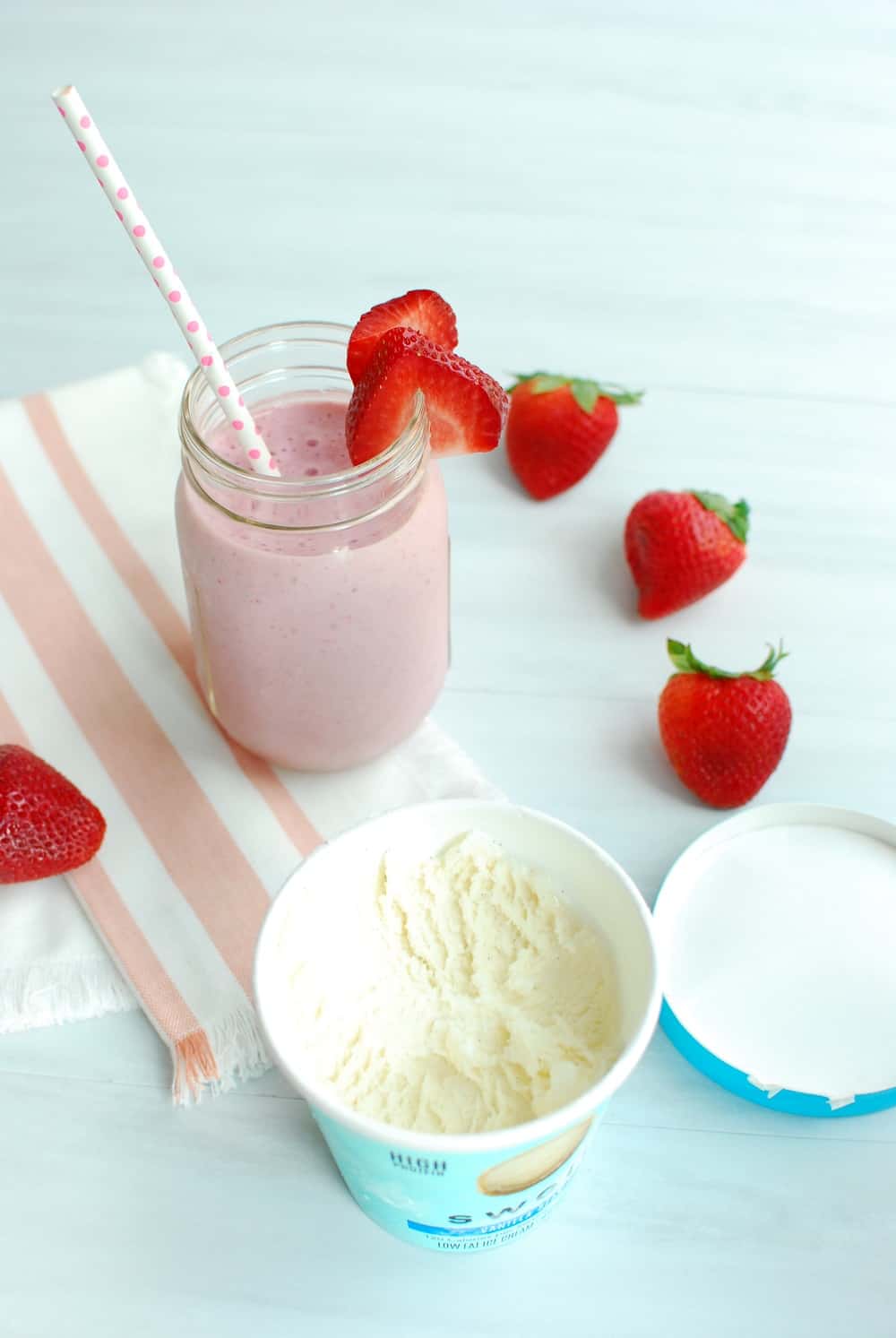 Open pint of ice cream next to a healthy strawberry milkshake