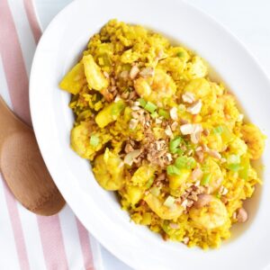 A oval bowl filled with pineapple fried rice next to a wooden spoon.