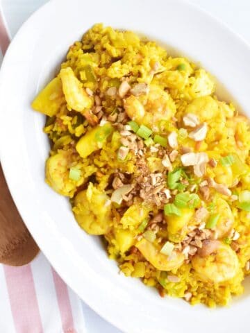 A oval bowl filled with pineapple fried rice next to a wooden spoon.