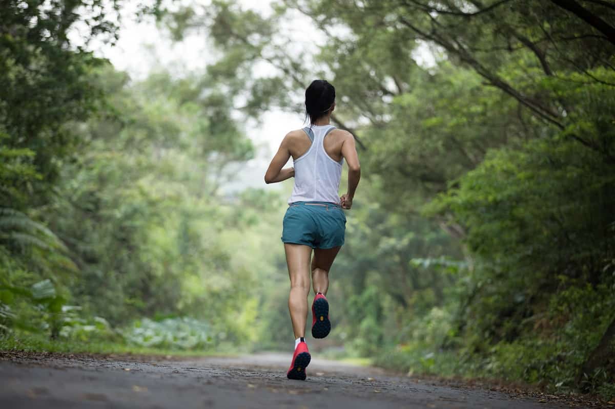 A woman running outside on a paved path in the woods.