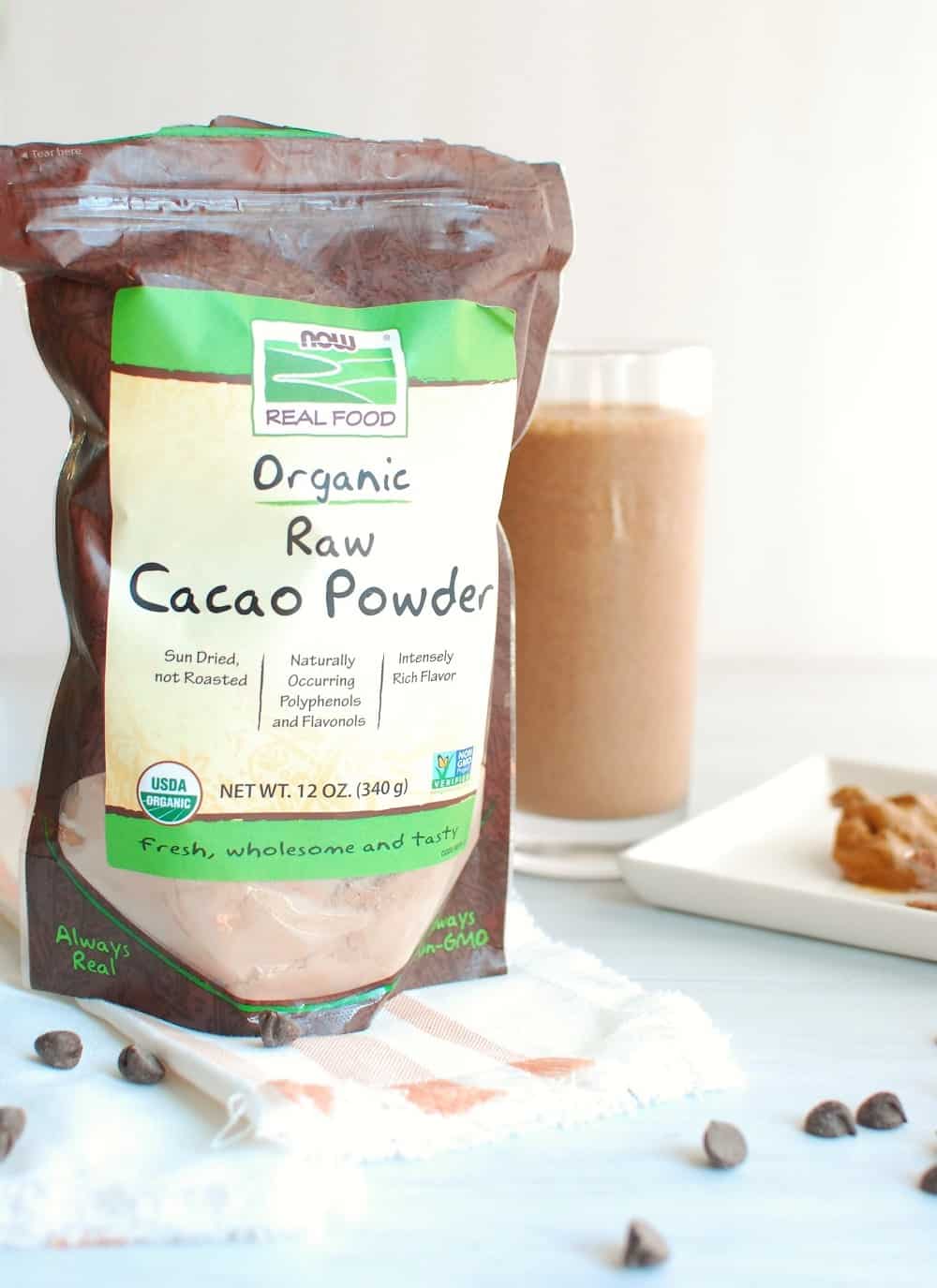 Bag of NOW Foods Cacao Powder next to a smoothie