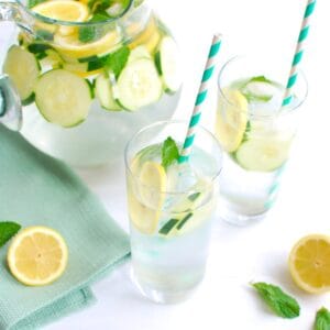 Two glasses of lemon mint cucumber water, with a pitcher in the background.