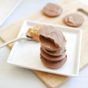 Several pieces of homemade peanut butter protein fudge on a plate next to a spoonful of peanut butter.