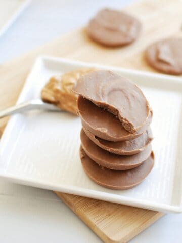 Several pieces of homemade peanut butter protein fudge on a plate next to a spoonful of peanut butter.
