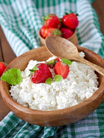 A wooden bowl with cottage cheese and strawberries next to a napkin.