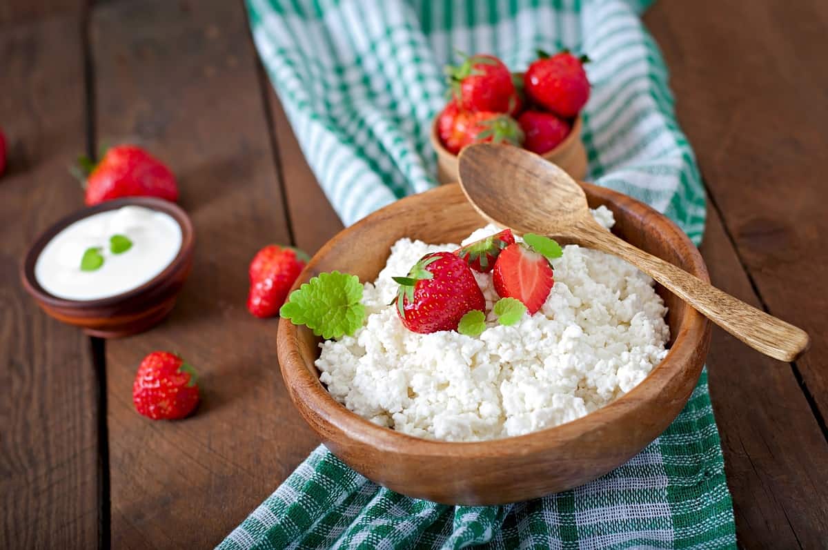 A wooden bowl of cottage cheese with a wooden spoon on a wooden table.