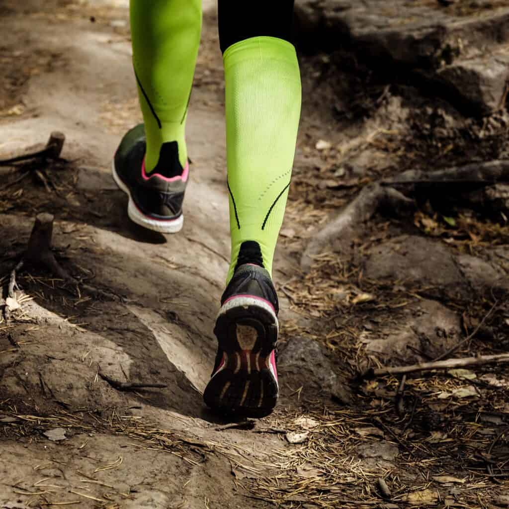 A woman's legs with compression socks on, running on a trail.