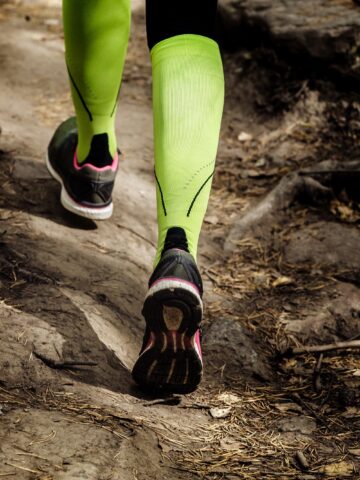 A woman's legs with compression socks on, running on a trail.