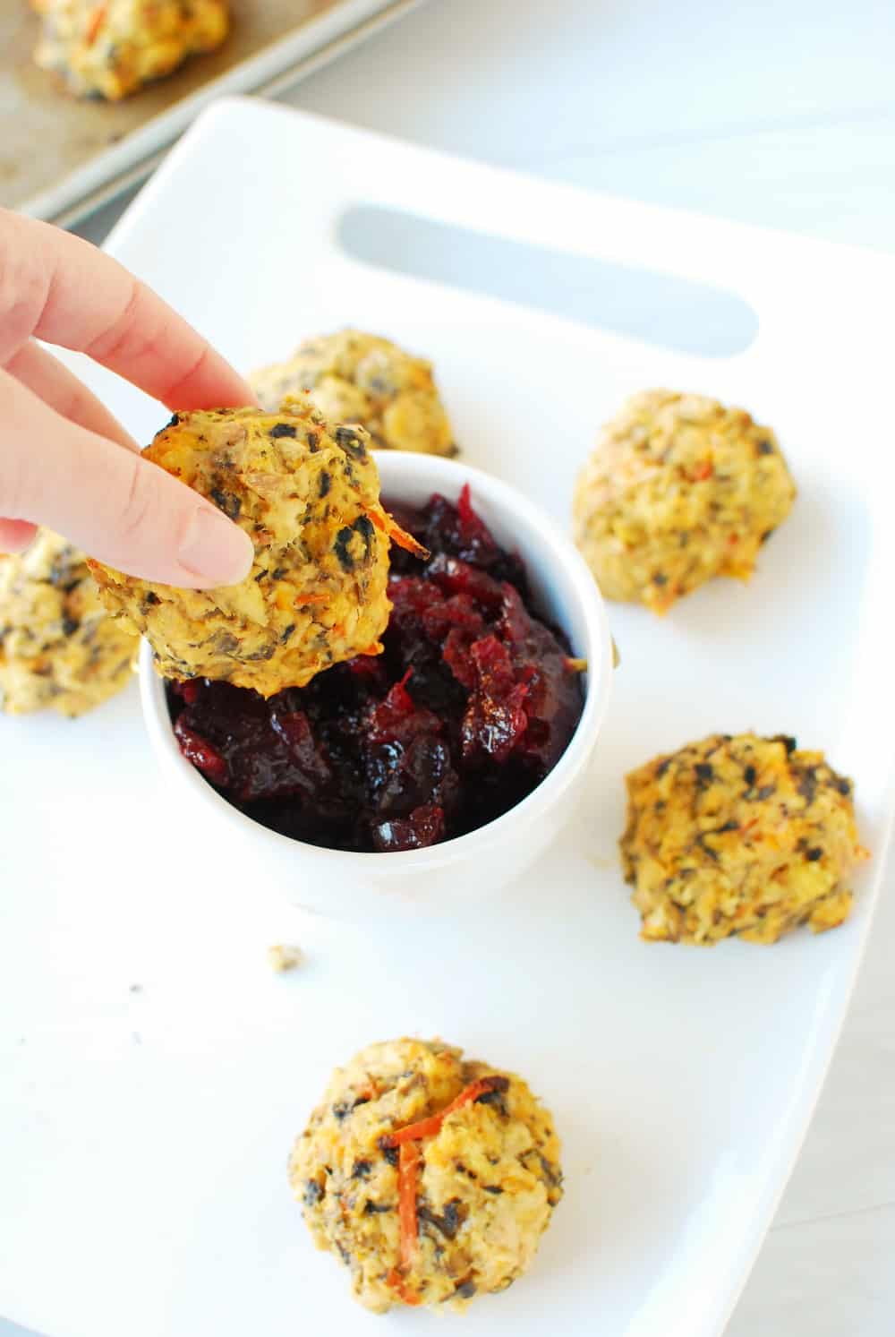 a hand dipping a healthy turkey meatball in cranberry sauce