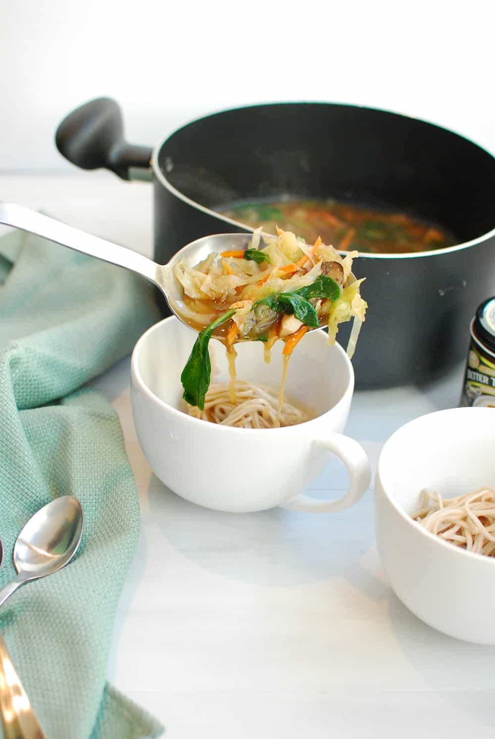 Ladling broth and vegetables over a bowl of soba noodles