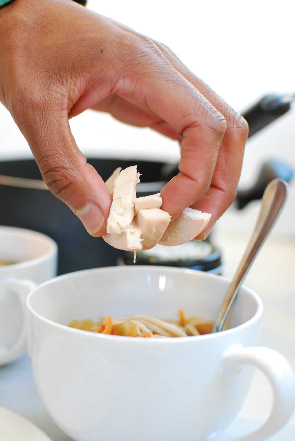 A hand placing chicken into a soba noodle broth bowl