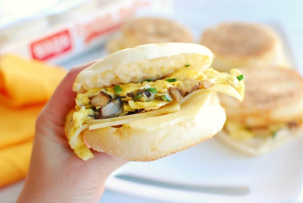 A woman's hand holding a vegetarian breakfast sandwich on an English mufifn.