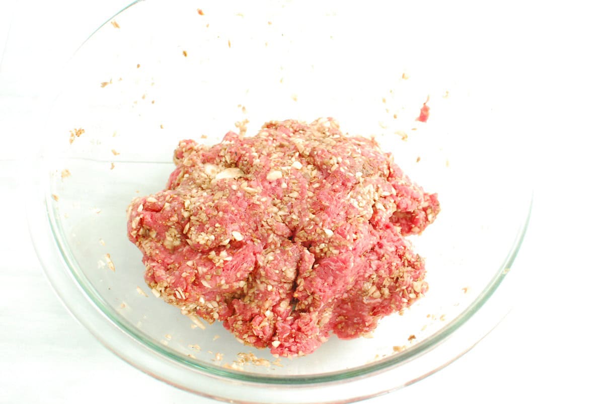 Beef mixed with mushrooms and seasonings in a mixing bowl.