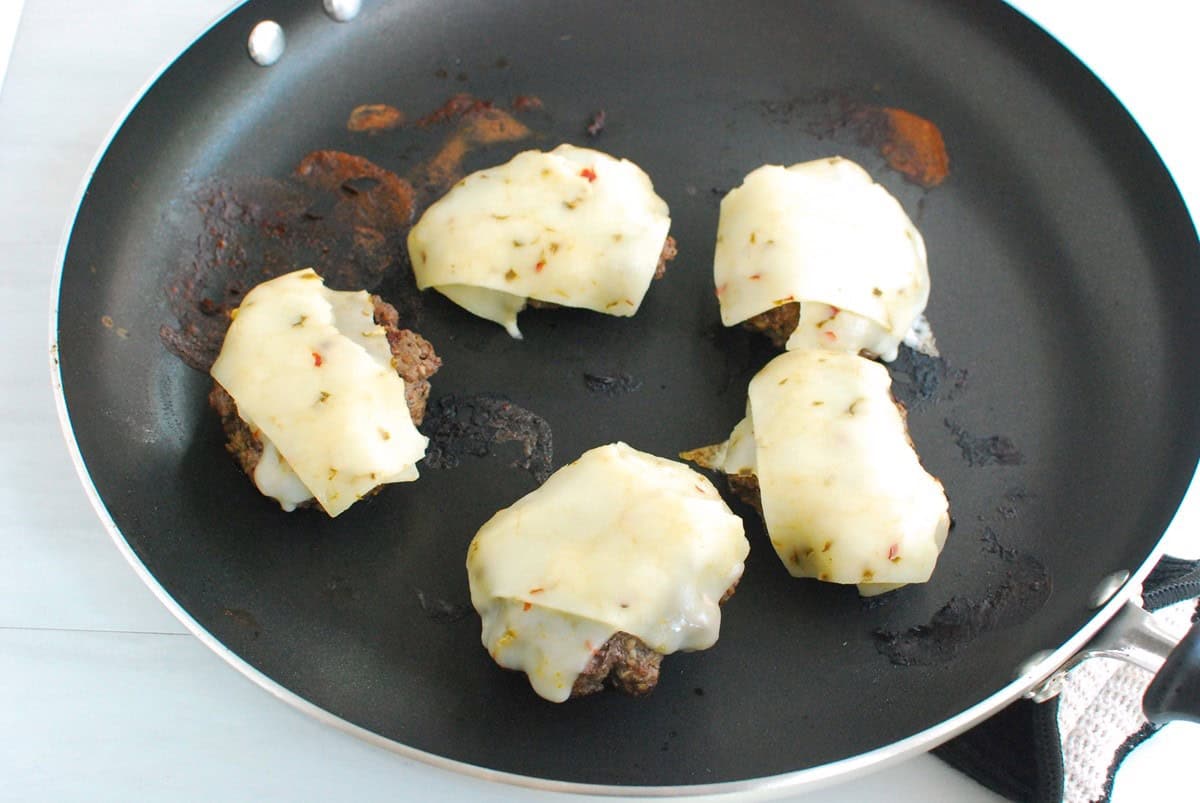 Cooked burgers in a skillet topped with cheese.