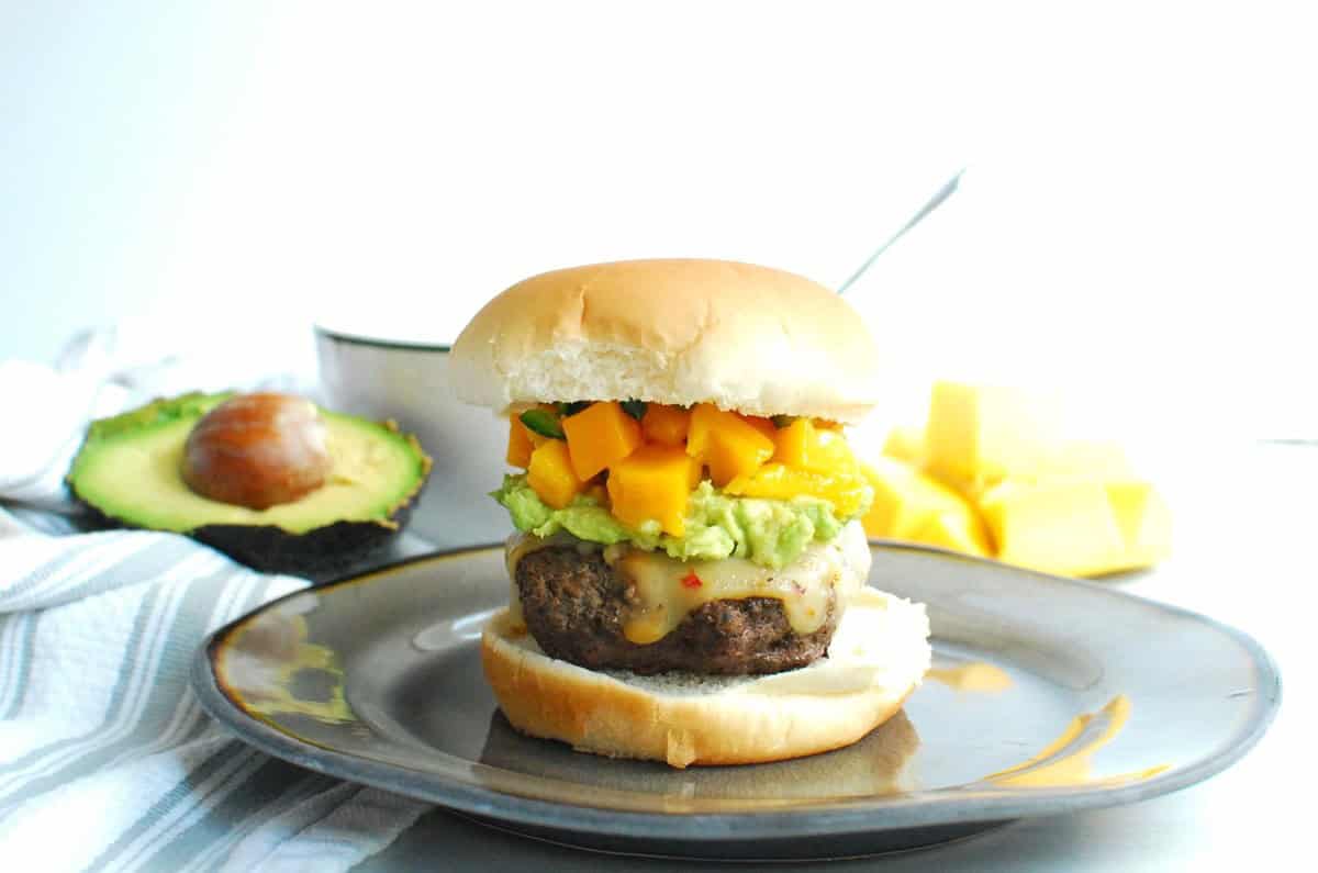 A lean beef and mushroom burger with mango salsa and mashed avocado, on a plate.