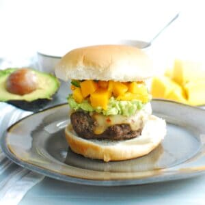 A beef burger topped with mashed avocado and mango salsa on a plate.