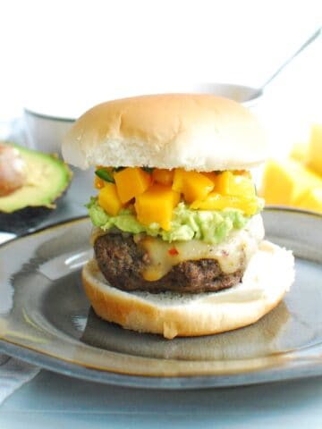 A beef burger topped with mashed avocado and mango salsa on a plate.