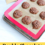 A tray full of double chocolate banana cookies next to a bag of cocoa powder