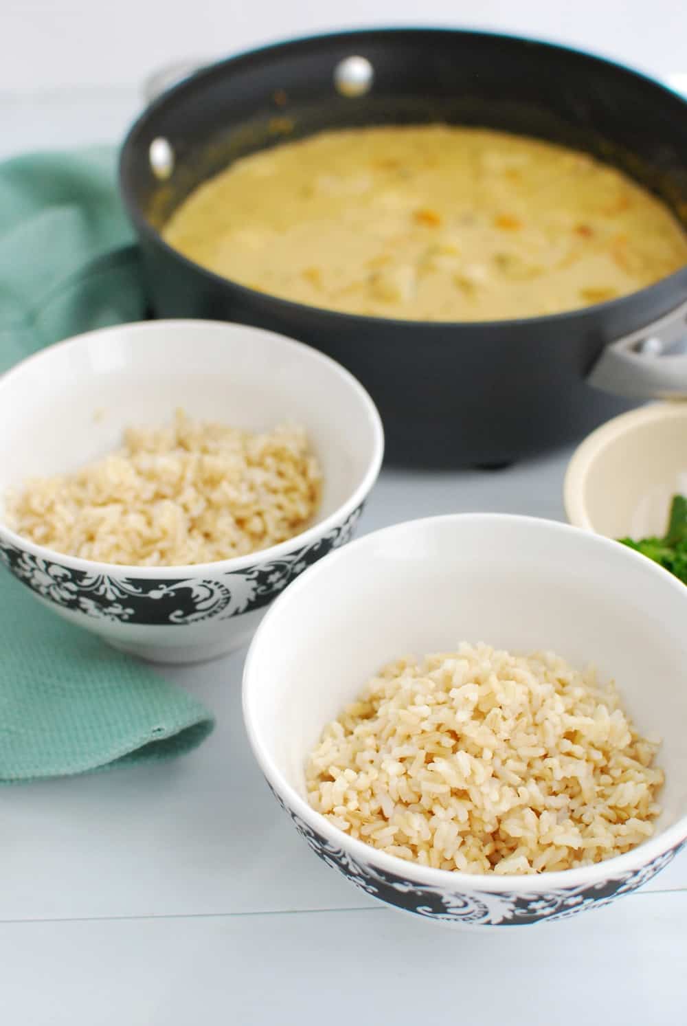 A pot of thai monkfish curry next to two bowls of brown rice